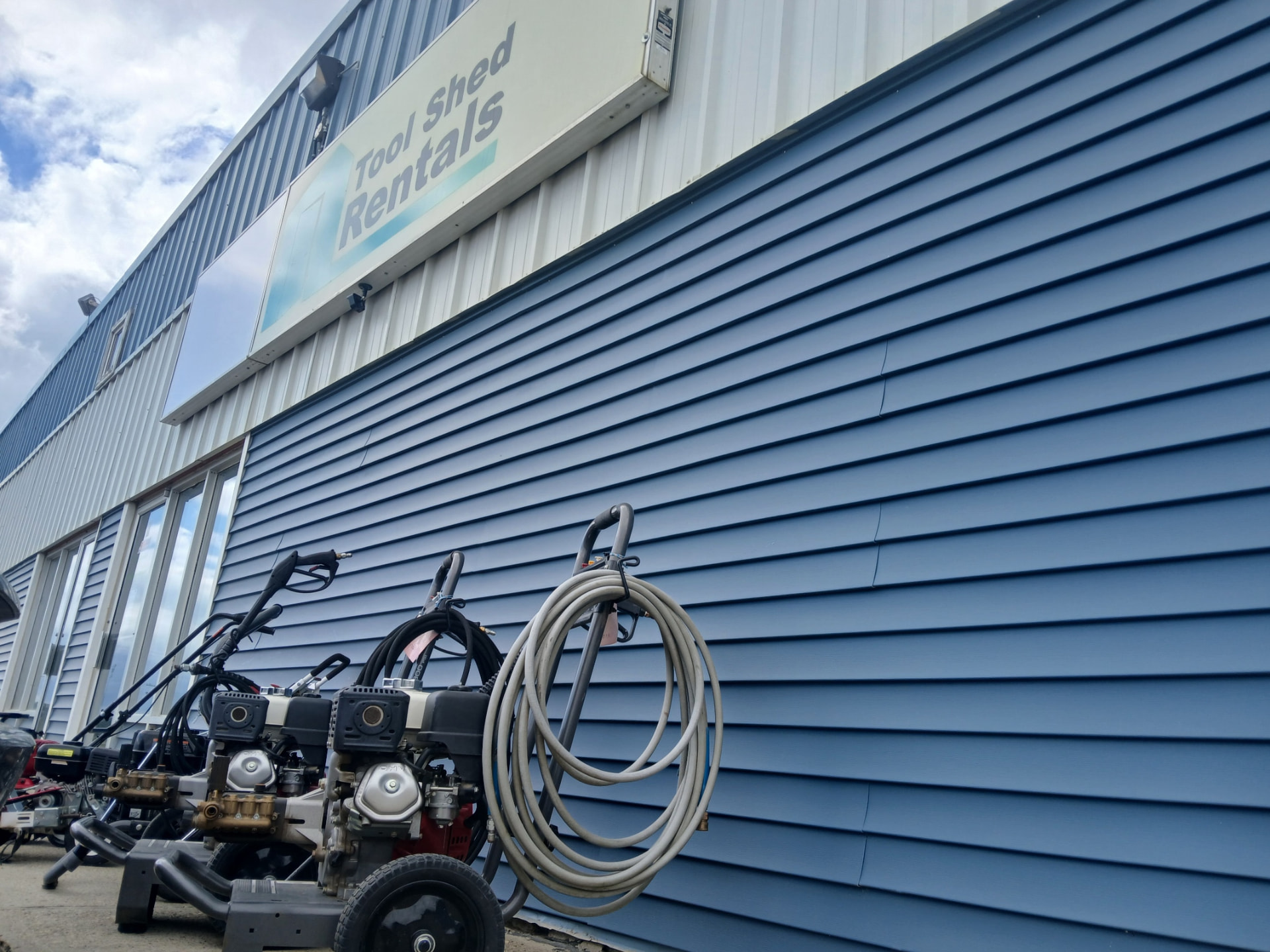 Row of pressure washers and hose reels along the Tool Shed Rentals shop wall